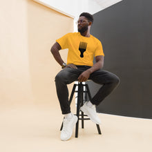 Load image into Gallery viewer, A man wearing a yellow crew neck t-shirt with a black graphic of an afro pick on the front, paired with blue jeans.