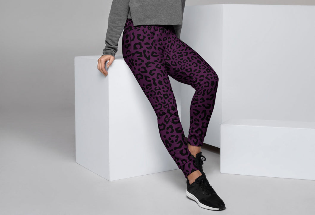 Woman wearing purple leopard print leggings and a gray sweater sitting on a white cube.